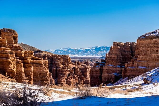 Red sandstone towers in Charyn Canyon with the snow line of the Tian Shan behind